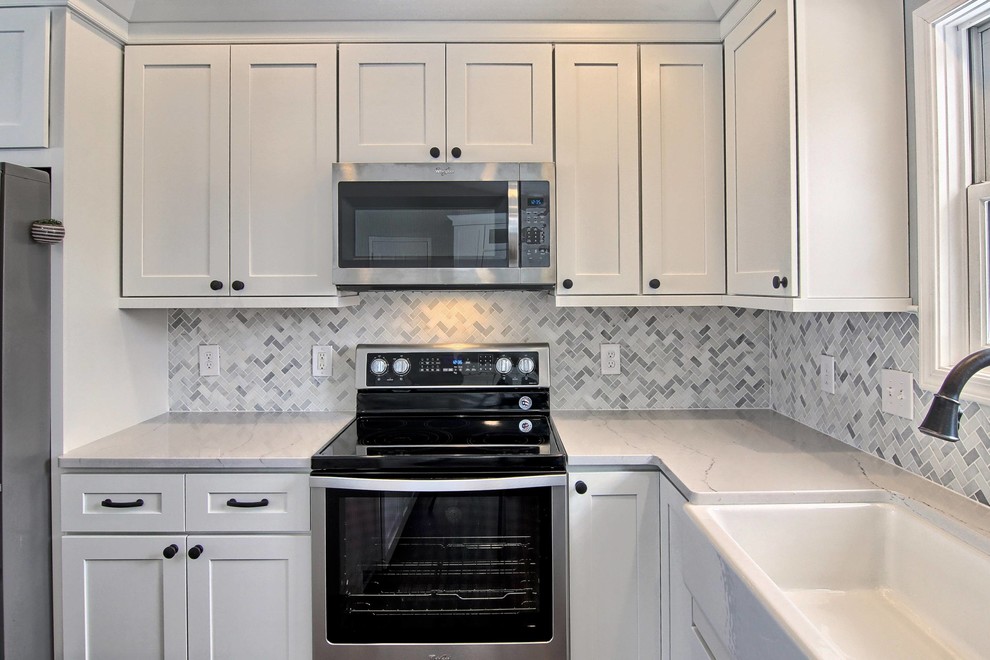 Mid-sized transitional l-shaped vinyl floor eat-in kitchen photo with a farmhouse sink, shaker cabinets, white cabinets, quartz countertops, white backsplash, stone tile backsplash, stainless steel appliances and an island
