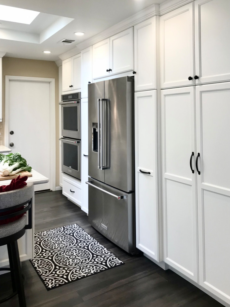 This is an example of a mid-sized traditional u-shaped open plan kitchen in San Diego with an undermount sink, flat-panel cabinets, white cabinets, quartz benchtops, beige splashback, subway tile splashback, stainless steel appliances, porcelain floors, with island, black floor, white benchtop and vaulted.