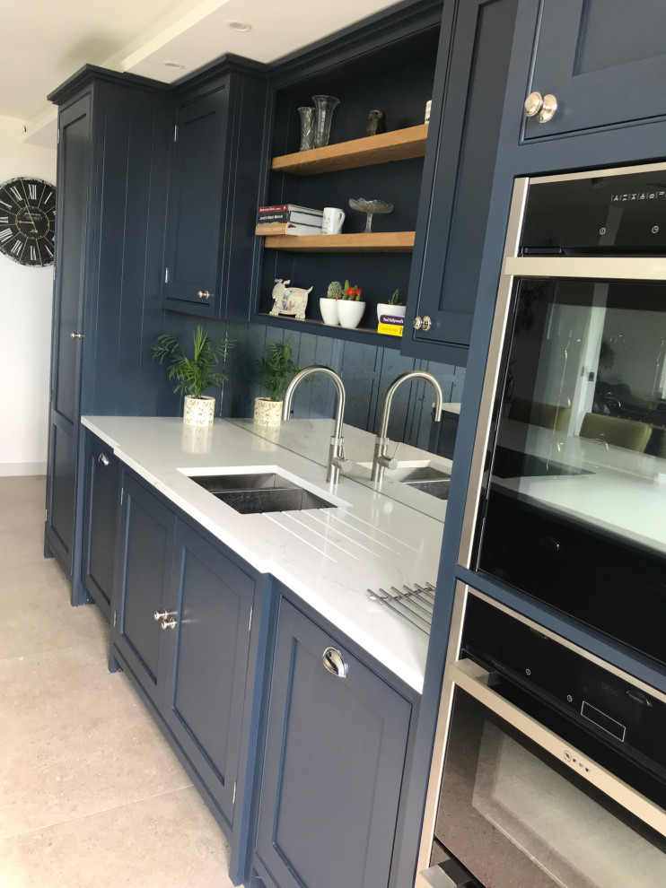 Mittelgroße Moderne Küche in L-Form mit Kassettenfronten, blauen Schränken, Küchenrückwand in Metallic, Kücheninsel und weißer Arbeitsplatte in Surrey