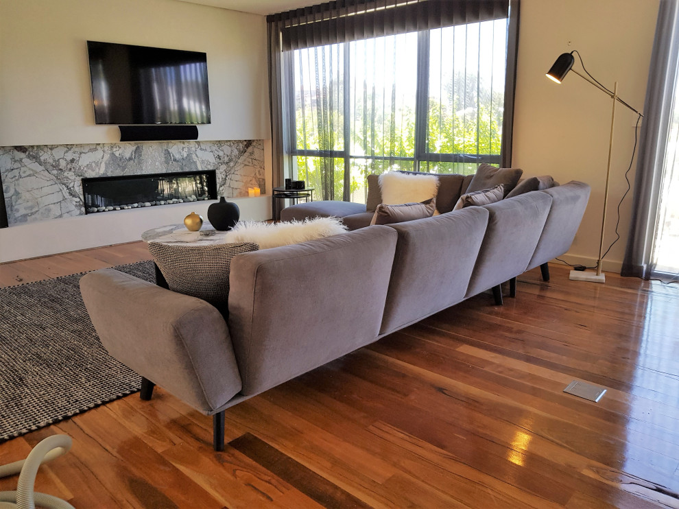 This is an example of a large modern formal living room in Perth with light hardwood flooring, a standard fireplace, a stone fireplace surround, a wall mounted tv and brown floors.