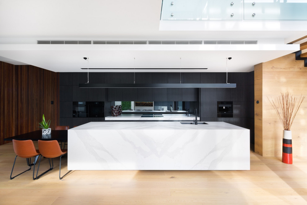 Inspiration for a contemporary eat-in kitchen in Melbourne with a double-bowl sink, flat-panel cabinets, black cabinets, mirror splashback, black appliances, light hardwood floors, with island and white benchtop.