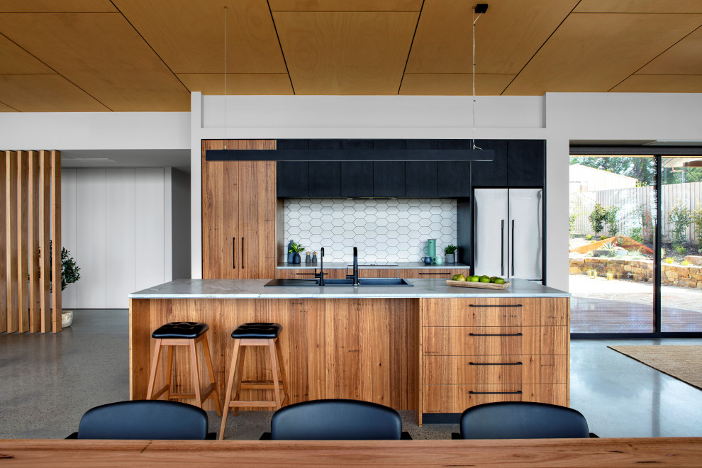 This is an example of a mid-sized contemporary galley open plan kitchen in Melbourne with a double-bowl sink, medium wood cabinets, marble benchtops, white splashback, mosaic tile splashback, black appliances, concrete floors, with island, grey floor and white benchtop.