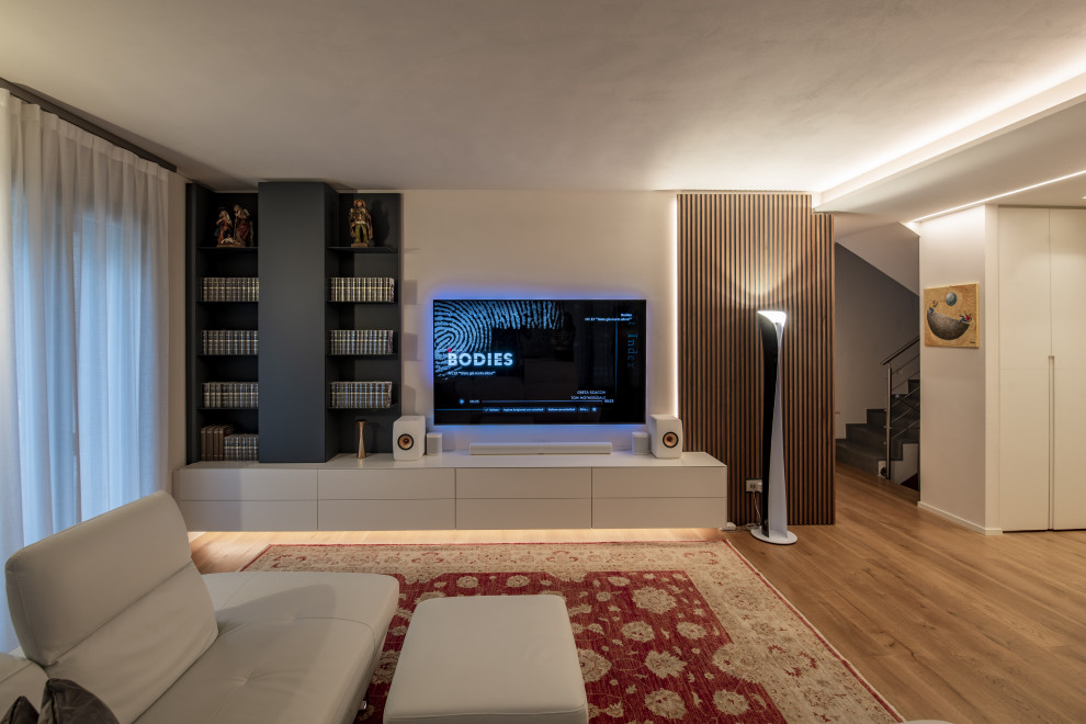 Пример оригинального дизайна: открытая гостиная комната среднего размера в стиле модернизм с с книжными шкафами и полками, бежевыми стенами, светлым паркетным полом, телевизором на стене, коричневым полом и многоуровневым потолком
