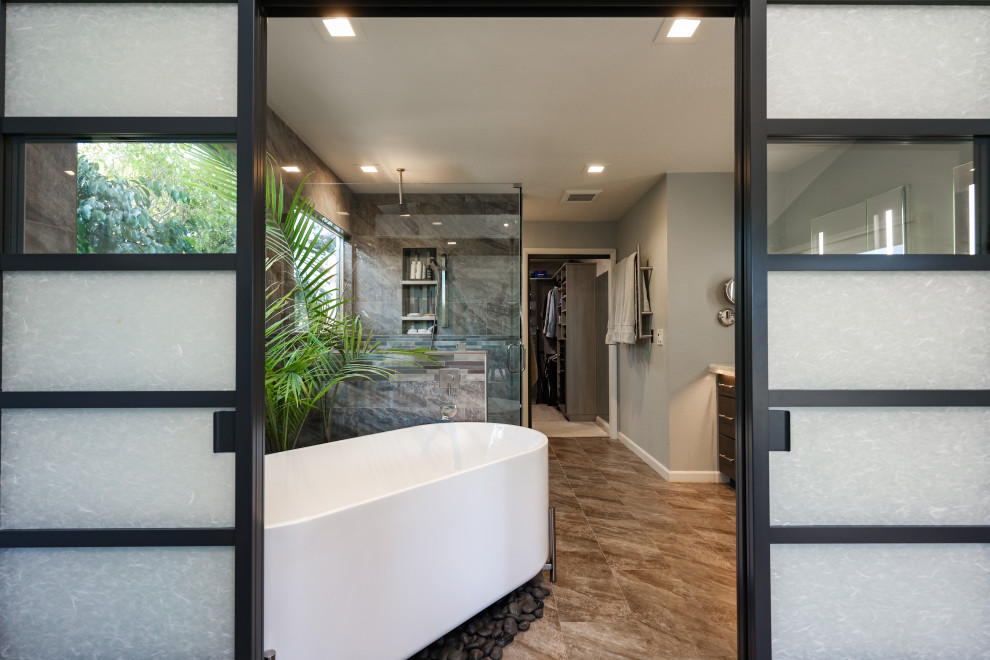 Photo of a large midcentury master bathroom in San Diego with flat-panel cabinets, dark wood cabinets, a freestanding tub, an open shower, a one-piece toilet, gray tile, porcelain tile, grey walls, porcelain floors, an undermount sink, onyx benchtops, multi-coloured floor, a hinged shower door, multi-coloured benchtops, a laundry, a double vanity and a built-in vanity.