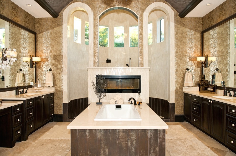 This is an example of an expansive modern master bathroom in Phoenix with an undermount sink, raised-panel cabinets, dark wood cabinets, marble benchtops, a drop-in tub, an open shower, beige tile, beige walls and travertine floors.