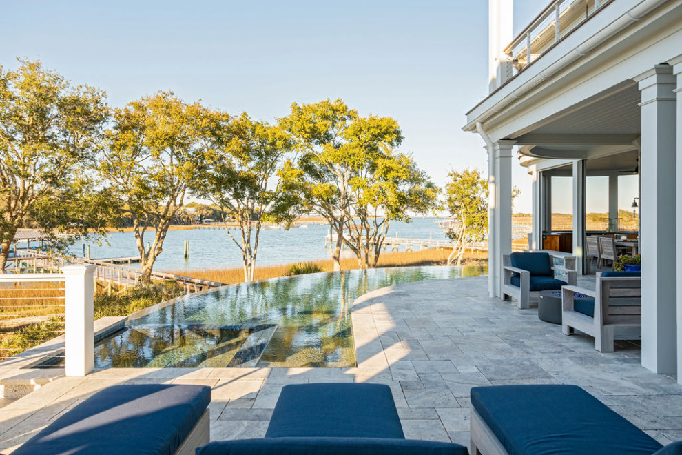 Immagine di un'ampia piscina a sfioro infinito stile marinaro personalizzata dietro casa con paesaggistica bordo piscina e pavimentazioni in pietra naturale