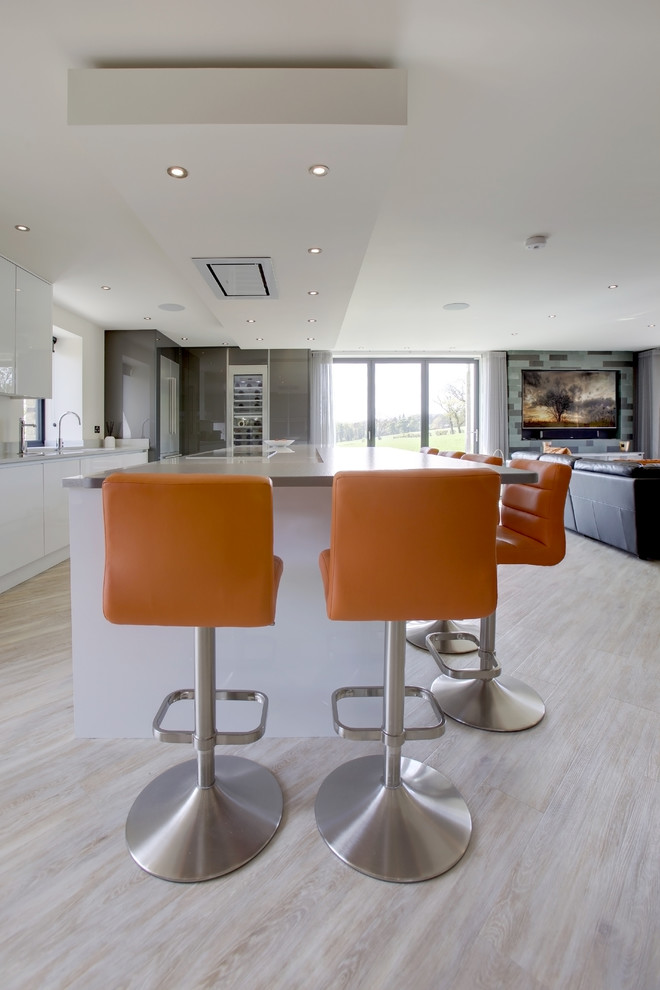 Inspiration for a large modern u-shaped open plan kitchen with a double-bowl sink, flat-panel cabinets, white cabinets, quartz worktops, grey splashback, stone tiled splashback, stainless steel appliances, light hardwood flooring and a breakfast bar.