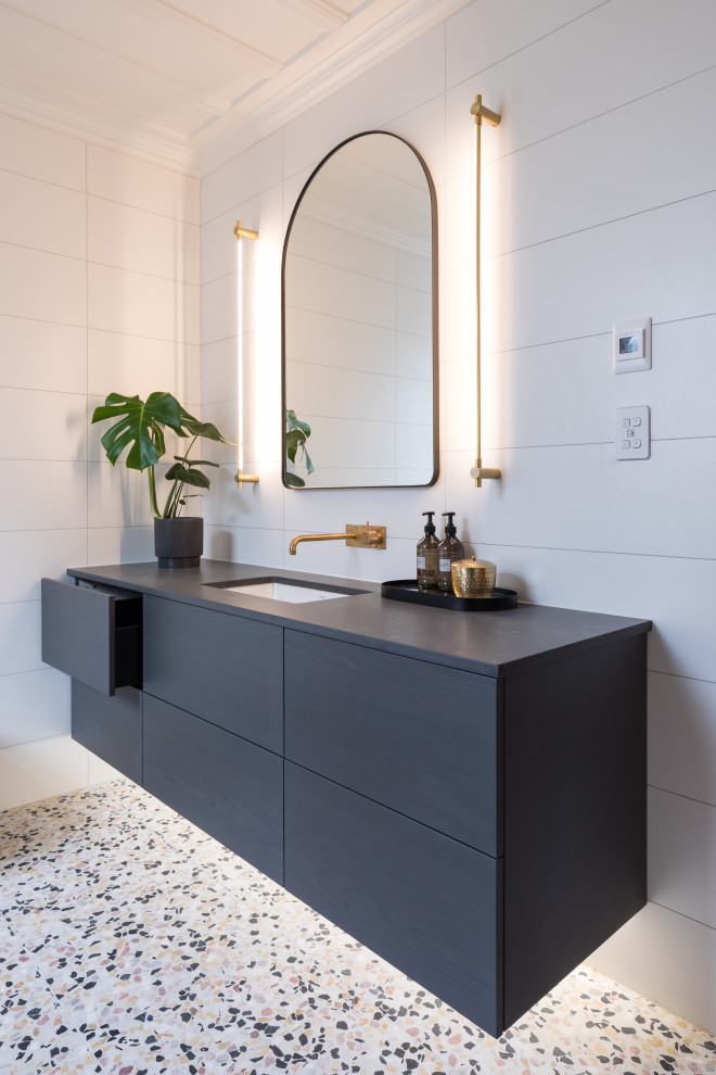 This is an example of a small contemporary kids wet room bathroom in Auckland with furniture-like cabinets, dark wood cabinets, a freestanding tub, a wall-mount toilet, pink tile, ceramic tile, pink walls, cement tiles, an undermount sink, engineered quartz benchtops, multi-coloured floor, a hinged shower door, grey benchtops, a niche, a single vanity, a floating vanity, exposed beam and decorative wall panelling.