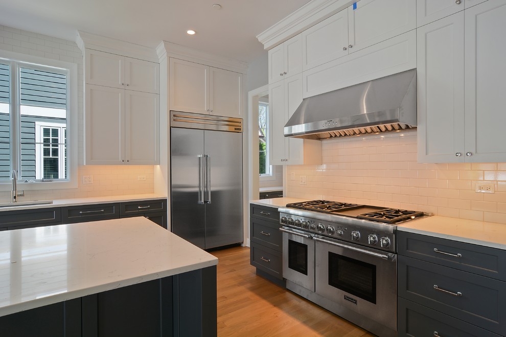 Large transitional l-shaped light wood floor open concept kitchen photo in Chicago with a single-bowl sink, shaker cabinets, gray cabinets, quartzite countertops, white backsplash, ceramic backsplash, stainless steel appliances and an island