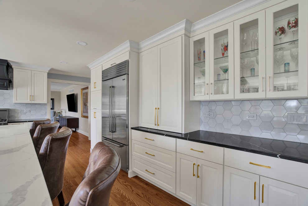 Photo of a mid-sized transitional l-shaped eat-in kitchen in Chicago with a drop-in sink, raised-panel cabinets, grey cabinets, quartz benchtops, stainless steel appliances, medium hardwood floors, with island and multi-coloured benchtop.