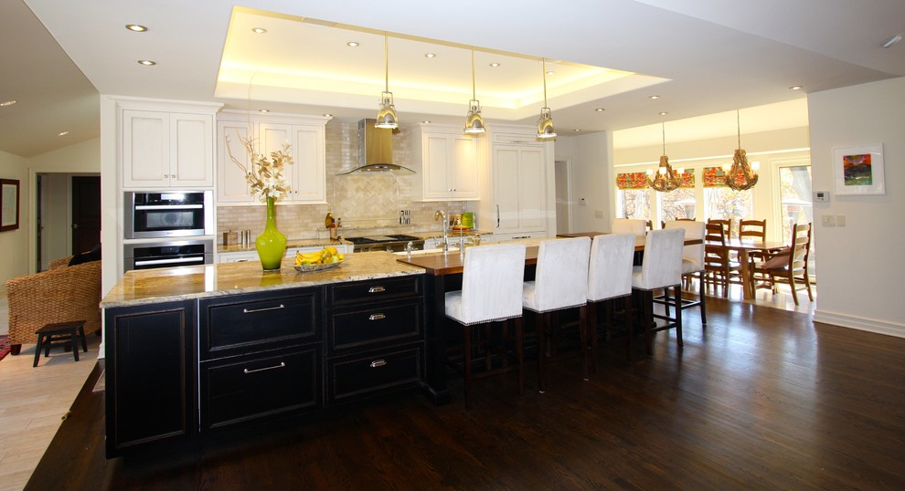 Example of a large transitional single-wall dark wood floor and brown floor open concept kitchen design in Kansas City with a farmhouse sink, recessed-panel cabinets, white cabinets, granite countertops, beige backsplash, paneled appliances, an island and multicolored countertops