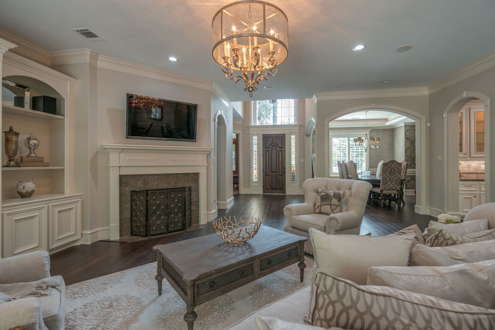 Design ideas for a mid-sized traditional open concept family room in Houston with beige walls, dark hardwood floors, no fireplace, a tile fireplace surround, a wall-mounted tv and grey floor.