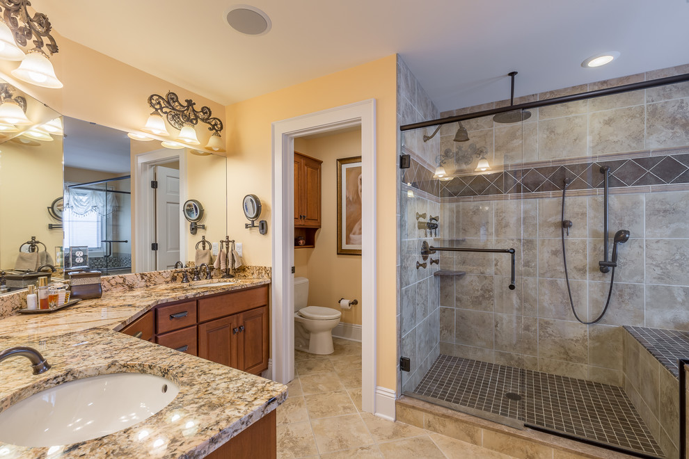 Design ideas for a traditional bathroom in Cleveland with raised-panel cabinets, medium wood cabinets, an alcove shower, a one-piece toilet, beige tile, brown tile, yellow walls, an undermount sink, granite benchtops, beige floor, a sliding shower screen and an enclosed toilet.