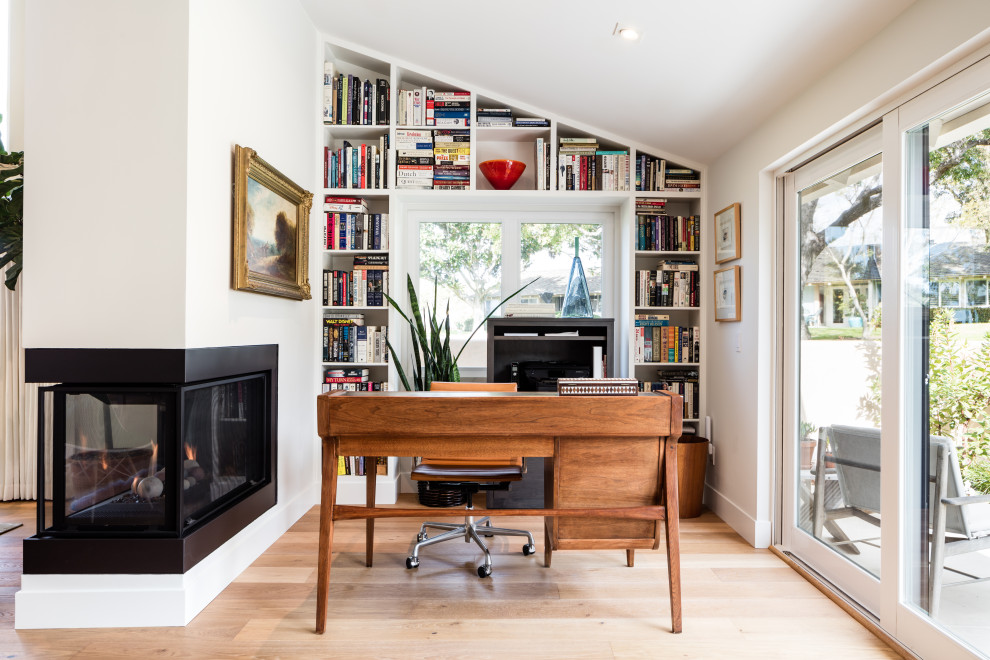 This is an example of a mid-sized contemporary home office in Orange County with white walls, light hardwood floors, a corner fireplace, a freestanding desk and beige floor.