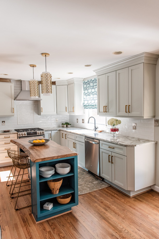 Transitional l-shaped medium tone wood floor and brown floor kitchen photo in Charlotte with recessed-panel cabinets, white cabinets, white backsplash, stainless steel appliances, an island and gray countertops