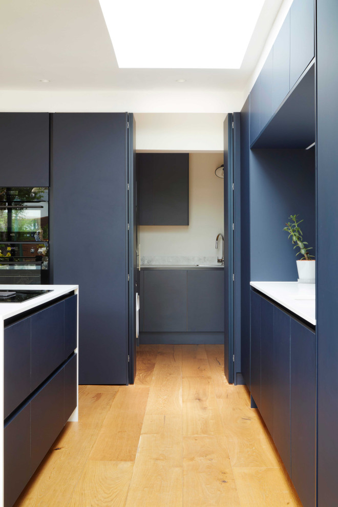 Exempel på ett mellanstort modernt vit vitt kök, med en undermonterad diskho, släta luckor, blå skåp, bänkskiva i kvartsit, vitt stänkskydd, svarta vitvaror, mellanmörkt trägolv och en köksö
