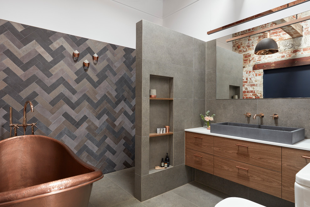 Inspiration for a large industrial master bathroom in Melbourne with flat-panel cabinets, a freestanding tub, an alcove shower, a one-piece toilet, gray tile, porcelain tile, white walls, porcelain floors, a vessel sink, engineered quartz benchtops, grey floor, an open shower, medium wood cabinets and white benchtops.