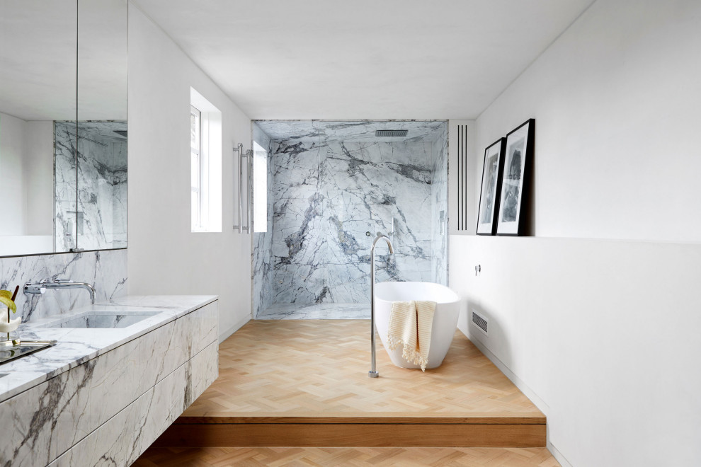 Inspiration for a contemporary bathroom in Melbourne with flat-panel cabinets, white cabinets, a freestanding tub, white tile, white walls, light hardwood floors, an undermount sink, beige floor and white benchtops.