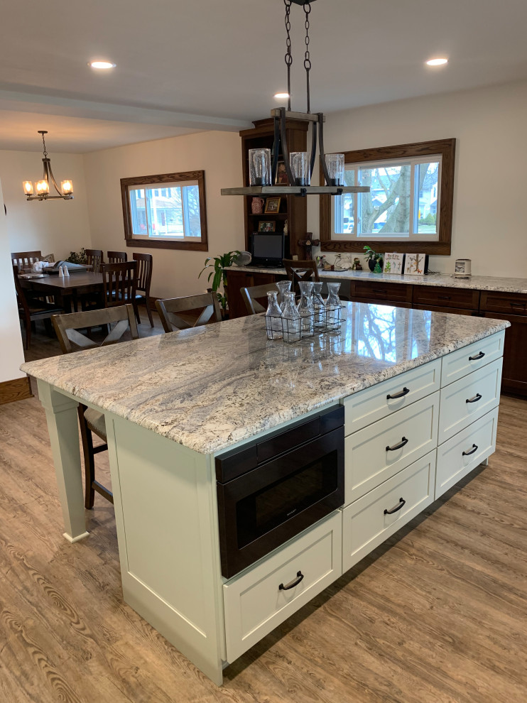 This is an example of a traditional u-shaped eat-in kitchen in Other with an undermount sink, shaker cabinets, medium wood cabinets, granite benchtops, white splashback, with island, brown floor and beige benchtop.