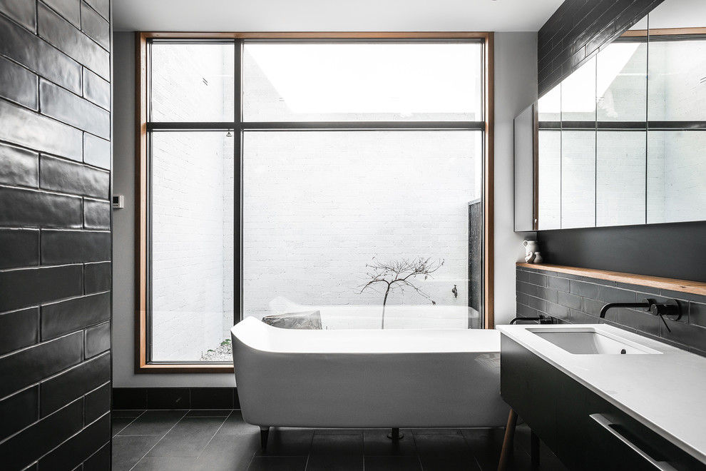 Photo of a mid-sized contemporary master wet room bathroom in Hobart with black cabinets, a freestanding tub, black tile, black walls, an undermount sink, black floor, white benchtops, a one-piece toilet, ceramic tile, ceramic floors, laminate benchtops, an open shower and flat-panel cabinets.