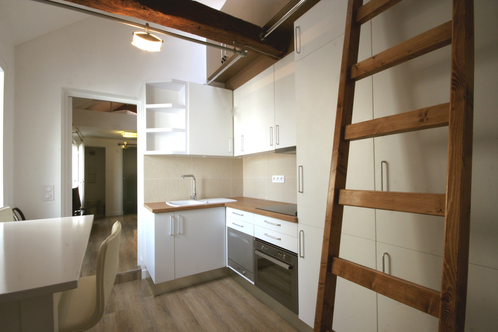 Cette image montre cuisine américaine in L With un évier 1 bac, des portes de placard blanches, un plan de travail en bois, une crédence beige, une crédence en céramique and un sol en bois brun.