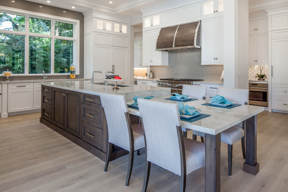 This is an example of an expansive transitional eat-in kitchen in Miami with a triple-bowl sink, shaker cabinets, white cabinets, granite benchtops, grey splashback, porcelain splashback, panelled appliances, light hardwood floors and with island.