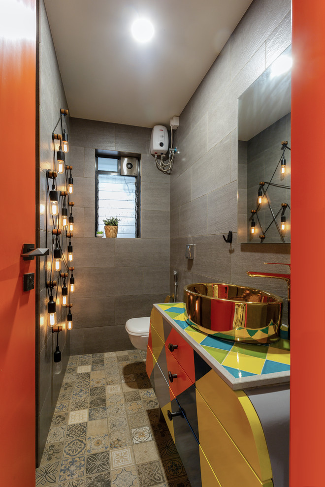 This is an example of an eclectic powder room in Mumbai with flat-panel cabinets, gray tile, cement tiles, a vessel sink, multi-coloured floor and multi-coloured benchtops.