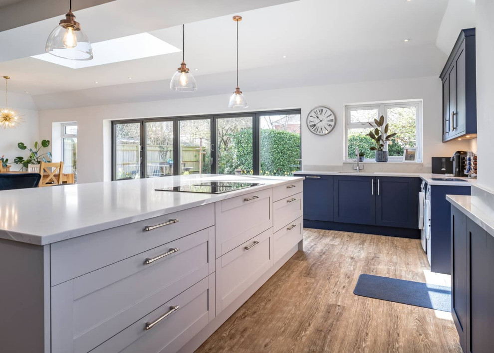 Inspiration for a large contemporary open plan kitchen in Oxfordshire with shaker cabinets, blue cabinets, quartzite benchtops, white splashback, light hardwood floors, with island, brown floor and white benchtop.