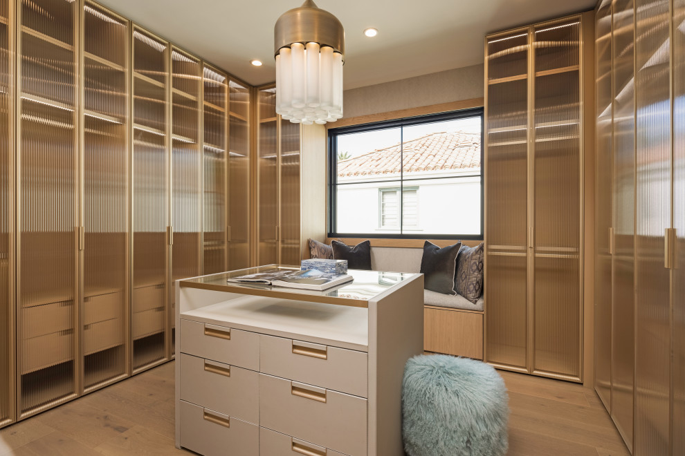Transitional women's walk-in wardrobe in Los Angeles with louvered cabinets and light wood cabinets.