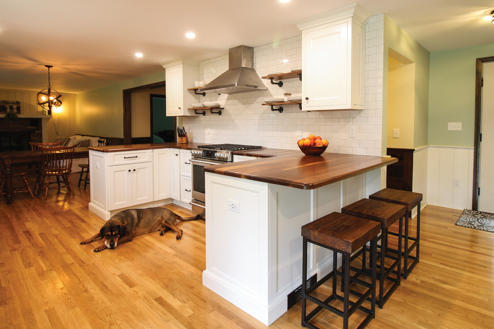 Inspiration for a mid-sized country u-shaped kitchen in Boston with a farmhouse sink, recessed-panel cabinets, white cabinets, wood benchtops, white splashback, subway tile splashback, stainless steel appliances, light hardwood floors, a peninsula, brown floor and brown benchtop.