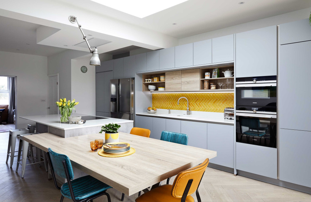 Large contemporary eat-in kitchen in London with flat-panel cabinets, grey cabinets, yellow splashback, ceramic splashback, with island and white benchtop.