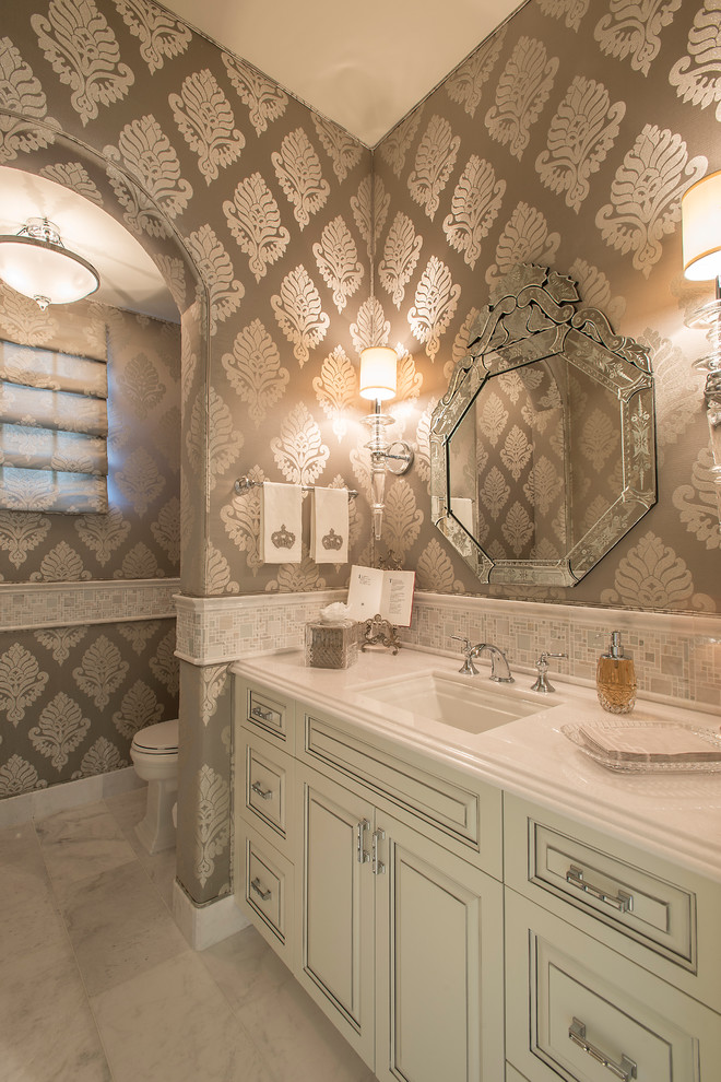 Inspiration for a mid-sized mediterranean powder room in Phoenix with an undermount sink, raised-panel cabinets, white cabinets, white tile, mosaic tile, multi-coloured walls, solid surface benchtops, a two-piece toilet and marble floors.