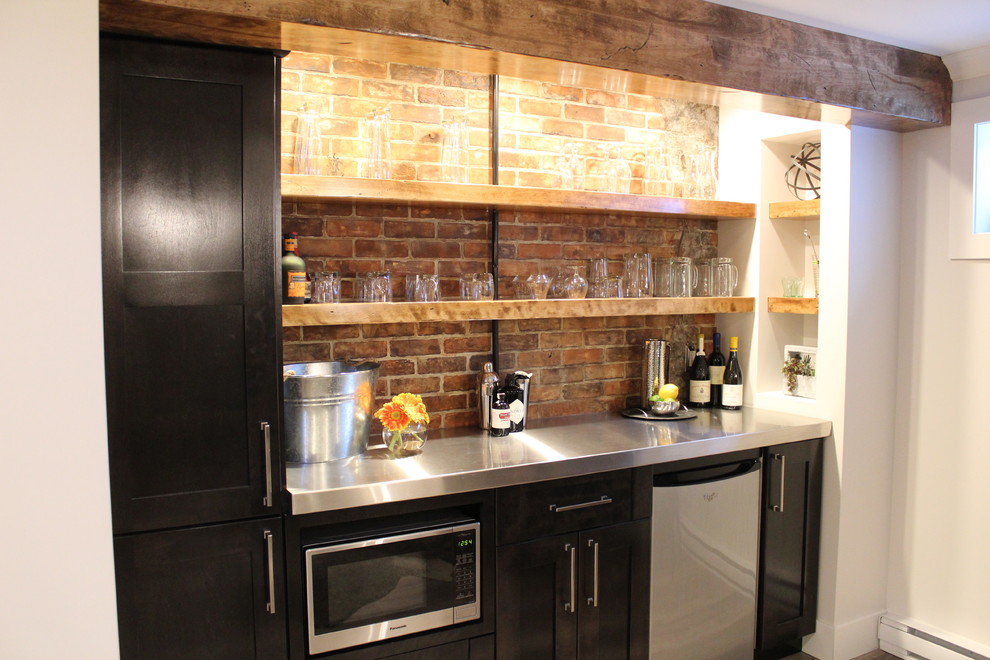 Design ideas for a modern home bar in Calgary with shaker cabinets, dark wood cabinets, stainless steel benchtops and brick splashback.