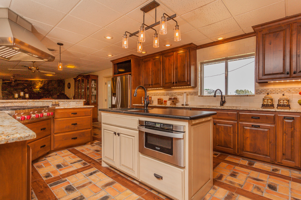Inspiration for a large rustic l-shaped brick floor eat-in kitchen remodel in Dallas with a double-bowl sink, raised-panel cabinets, medium tone wood cabinets, granite countertops, beige backsplash, ceramic backsplash, stainless steel appliances and two islands
