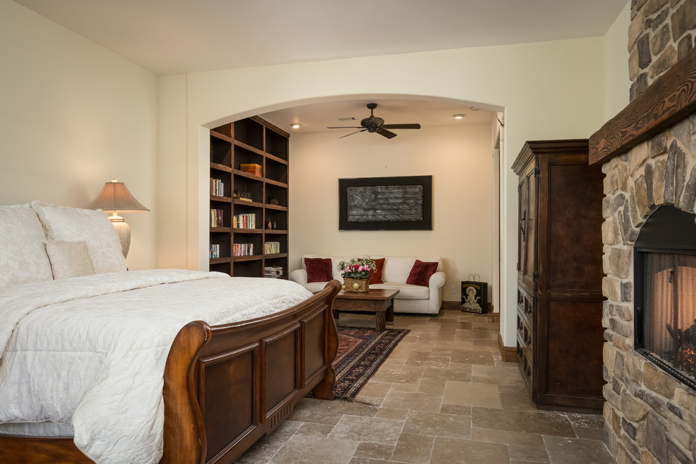 Photo of a mid-sized mediterranean master bedroom in San Francisco with beige walls, ceramic floors, a standard fireplace, a stone fireplace surround and beige floor.