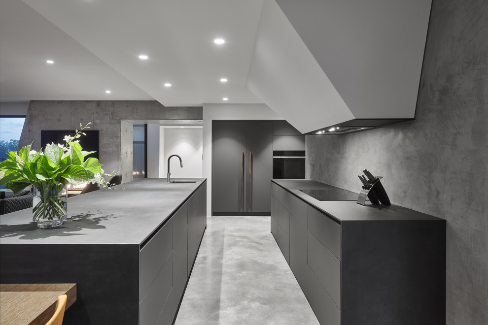 Large modern l-shaped open plan kitchen in Perth with concrete benchtops, grey splashback, stone slab splashback, concrete floors, with island, grey floor, grey benchtop, an undermount sink, flat-panel cabinets, grey cabinets and panelled appliances.