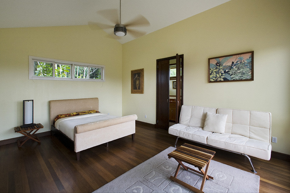 This is an example of a mid-sized tropical guest bedroom in New York with yellow walls, dark hardwood floors and brown floor.