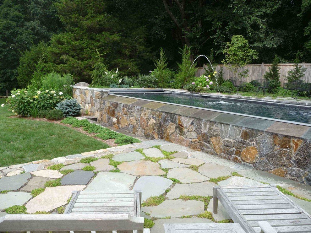 This is an example of a modern backyard rectangular infinity pool in Bridgeport with a water feature and natural stone pavers.