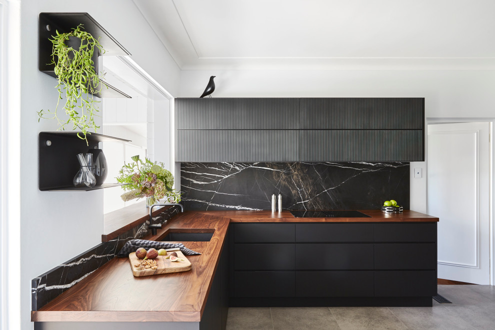 Mid-sized contemporary l-shaped separate kitchen in Sydney with a single-bowl sink, flat-panel cabinets, black cabinets, wood benchtops, black splashback, marble splashback, black appliances, porcelain floors, no island, grey floor and brown benchtop.