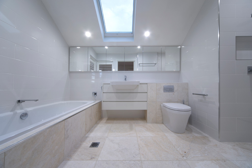 Inspiration for a mid-sized traditional kids bathroom in Canberra - Queanbeyan with glass-front cabinets, white cabinets, a drop-in tub, an alcove shower, a one-piece toilet, beige tile, stone tile, white walls, travertine floors, an integrated sink and terrazzo benchtops.