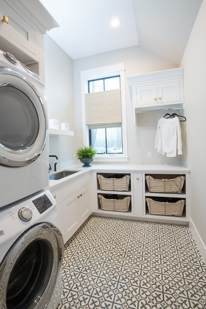 Mid-sized modern l-shaped dedicated laundry room in Other with an undermount sink, shaker cabinets, white cabinets, quartz benchtops, grey walls, concrete floors, a stacked washer and dryer, grey floor and white benchtop.