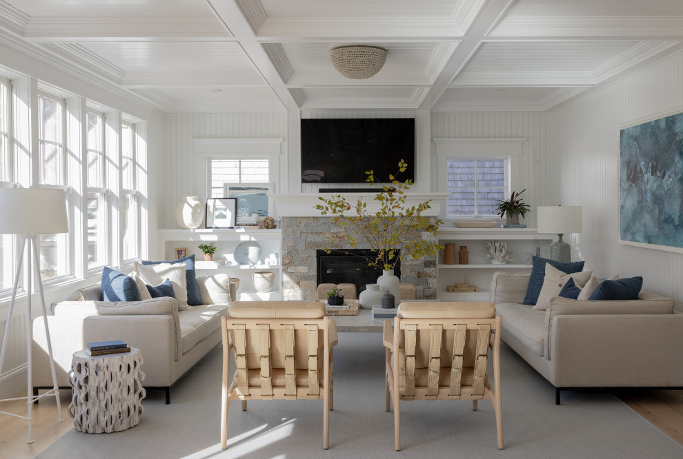 На фото: гостиная комната в морском стиле с белыми стенами, паркетным полом среднего тона, стандартным камином, фасадом камина из каменной кладки, телевизором на стене, коричневым полом и кессонным потолком с
