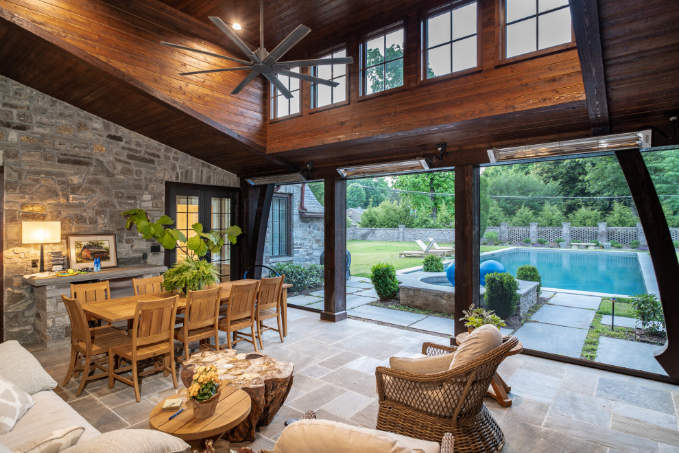Expansive traditional back patio in Other with natural stone paving and a roof extension.