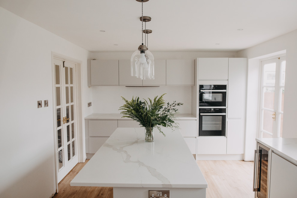 Mid-sized modern eat-in kitchen in Other with an undermount sink, flat-panel cabinets, grey cabinets, quartzite benchtops, white splashback, black appliances, laminate floors, with island, brown floor and white benchtop.