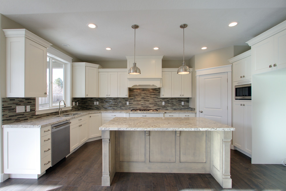 Photo of a large transitional u-shaped open plan kitchen in Salt Lake City with an undermount sink, recessed-panel cabinets, white cabinets, granite benchtops, beige splashback, matchstick tile splashback, stainless steel appliances, dark hardwood floors, with island and brown floor.