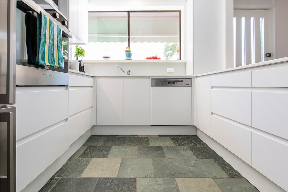 Inspiration for a mid-sized modern u-shaped eat-in kitchen in Sydney with an undermount sink, flat-panel cabinets, white cabinets, quartz benchtops, white splashback, glass sheet splashback, stainless steel appliances, slate floors, a peninsula, blue floor and white benchtop.