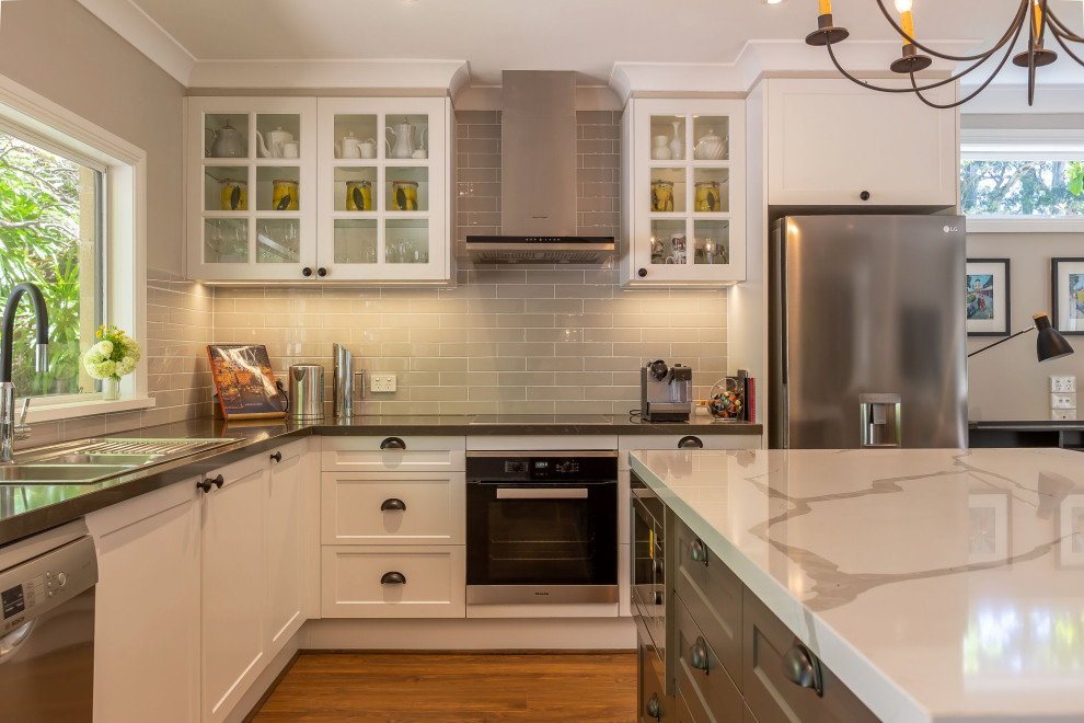 Inspiration for a traditional l-shaped open plan kitchen with a double-bowl sink, shaker cabinets, white cabinets, quartz benchtops, grey splashback, subway tile splashback, stainless steel appliances, vinyl floors, with island, brown floor and grey benchtop.