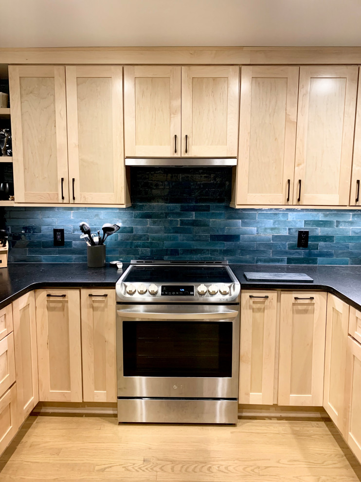 Mid-sized transitional u-shaped light wood floor and brown floor eat-in kitchen photo with an undermount sink, shaker cabinets, light wood cabinets, granite countertops, blue backsplash, ceramic backsplash, stainless steel appliances, a peninsula and black countertops