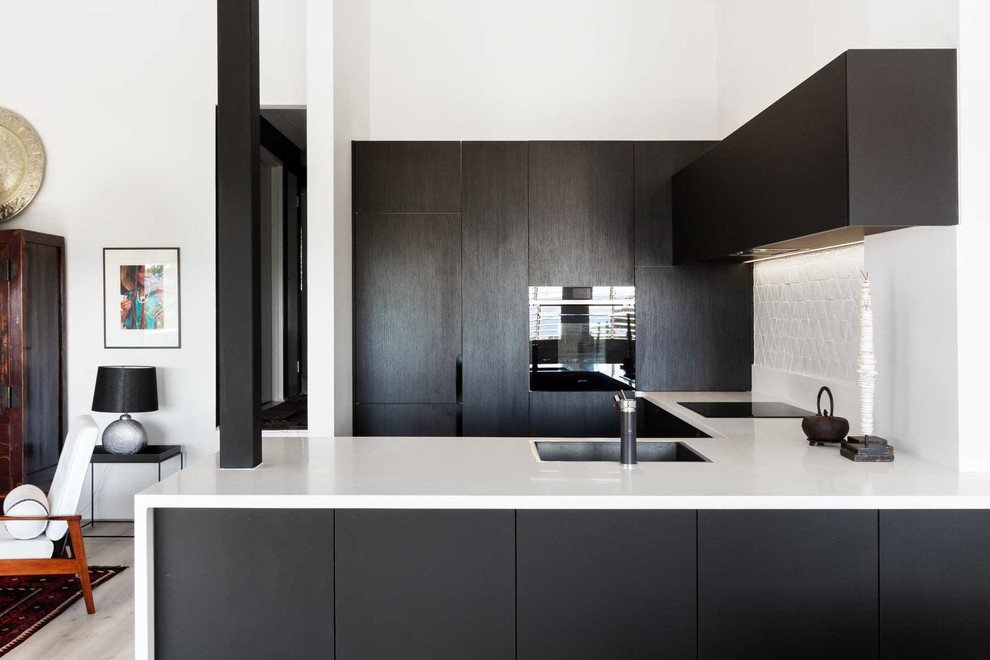 Design ideas for a small eclectic u-shaped eat-in kitchen in Sydney with a single-bowl sink, black cabinets, solid surface benchtops, white splashback, mosaic tile splashback, black appliances, laminate floors, grey floor and white benchtop.