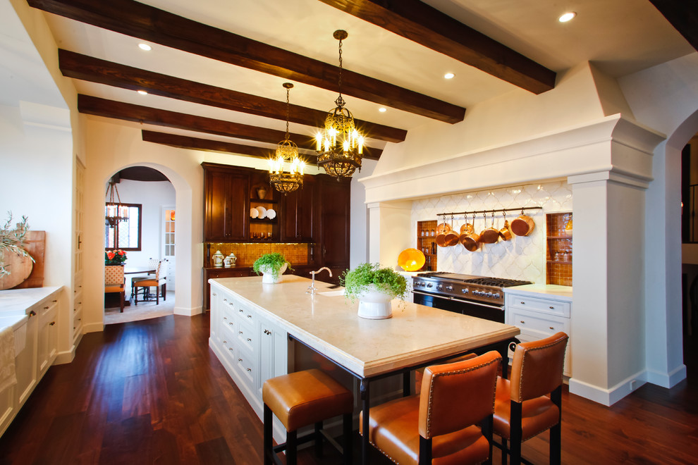 This is an example of a large mediterranean kitchen in Los Angeles with a farmhouse sink, recessed-panel cabinets, beige cabinets, limestone benchtops, orange splashback, ceramic splashback, panelled appliances, medium hardwood floors, with island, brown floor and beige benchtop.